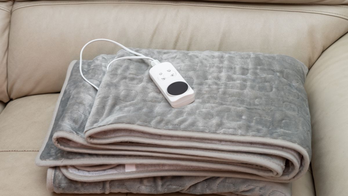 Eine elektrische Heizdecke liegt ordentlich gefaltet auf einem Sofa mit einer Fernbedienung.