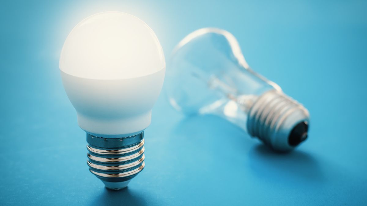 Eine LED-Lampe leuchtet neben einer herkömmlichen Glühbirne auf einem blauen Hintergrund.