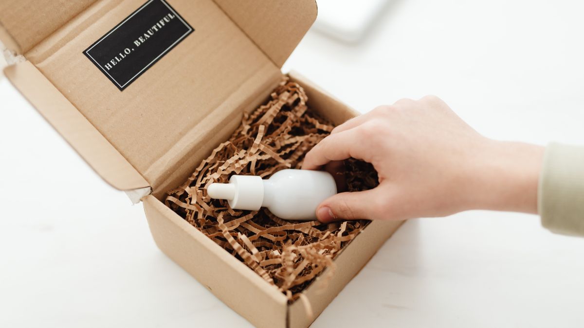 Eine Hand greift nach einer weißen Flasche in einer Kartonverpackung mit Füllmaterial.