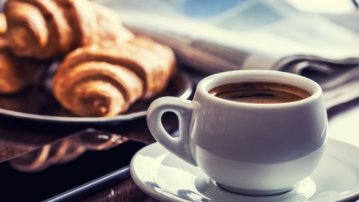 Eine Tasse Kaffee steht neben einem Teller mit Croissants und einem Smartphone.